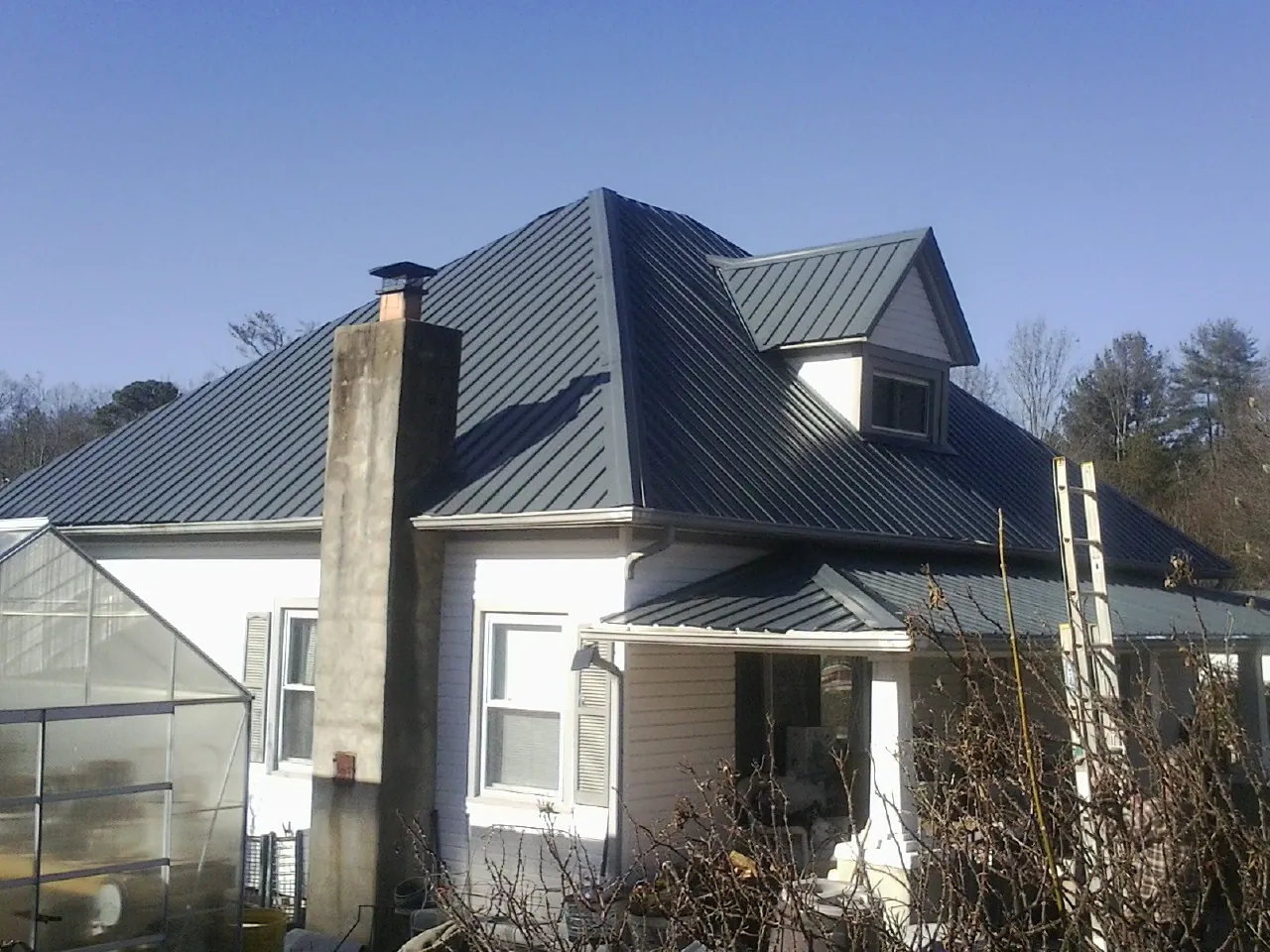 Dark blue standing seam metal roof on a white farmhouse with dormer — Slate & Tile Roof Repair by Roofing Brothers in Iota