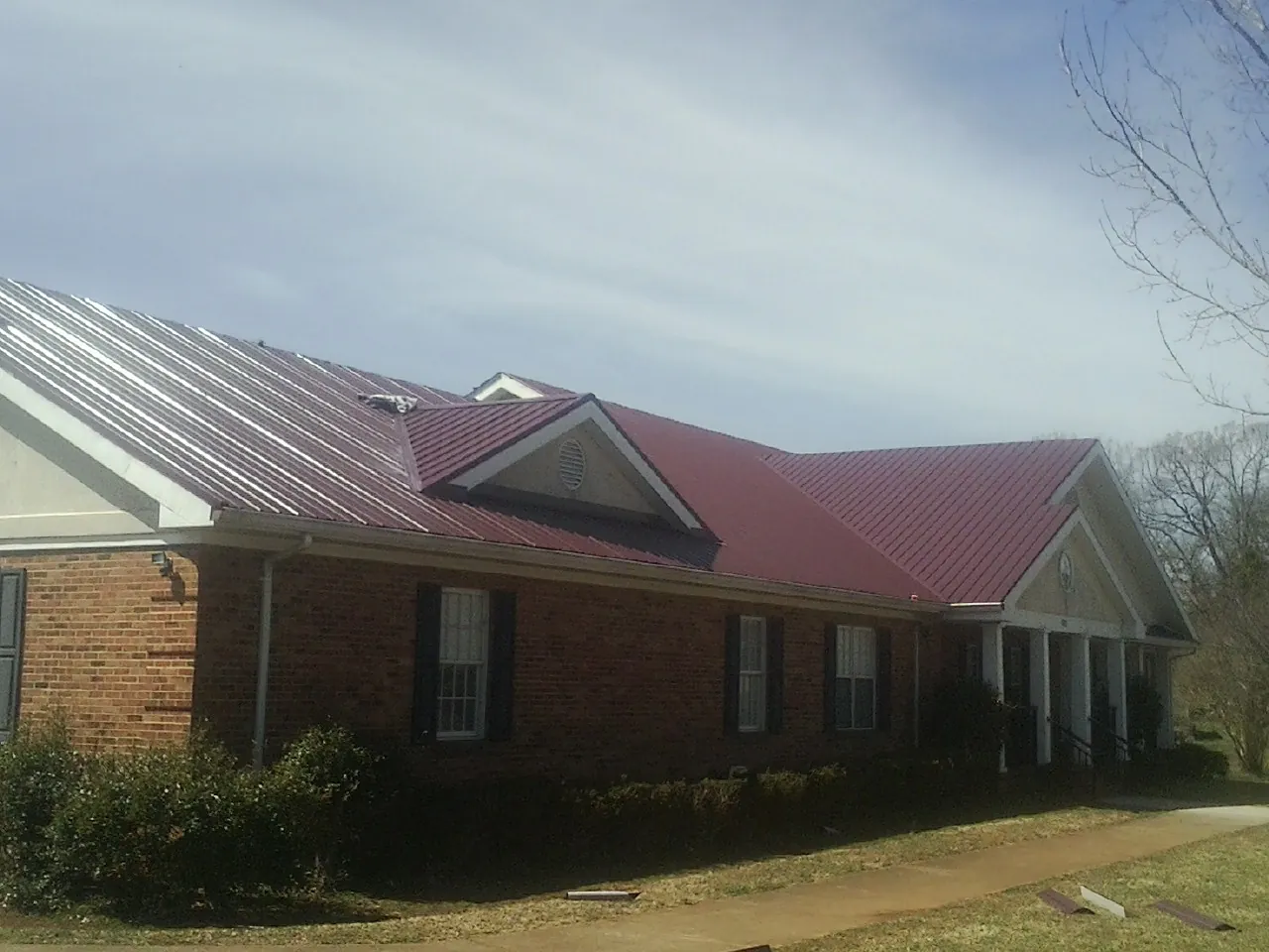 Red metal roof with gabled entries on a long brick building, from a Hail Damage Roof Repair job in Iota