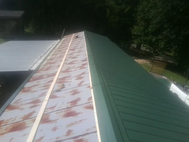 Old rusted panels beside newly installed green metal roofing — Wind Damage Roof Repair by Roofing Brothers in Iota