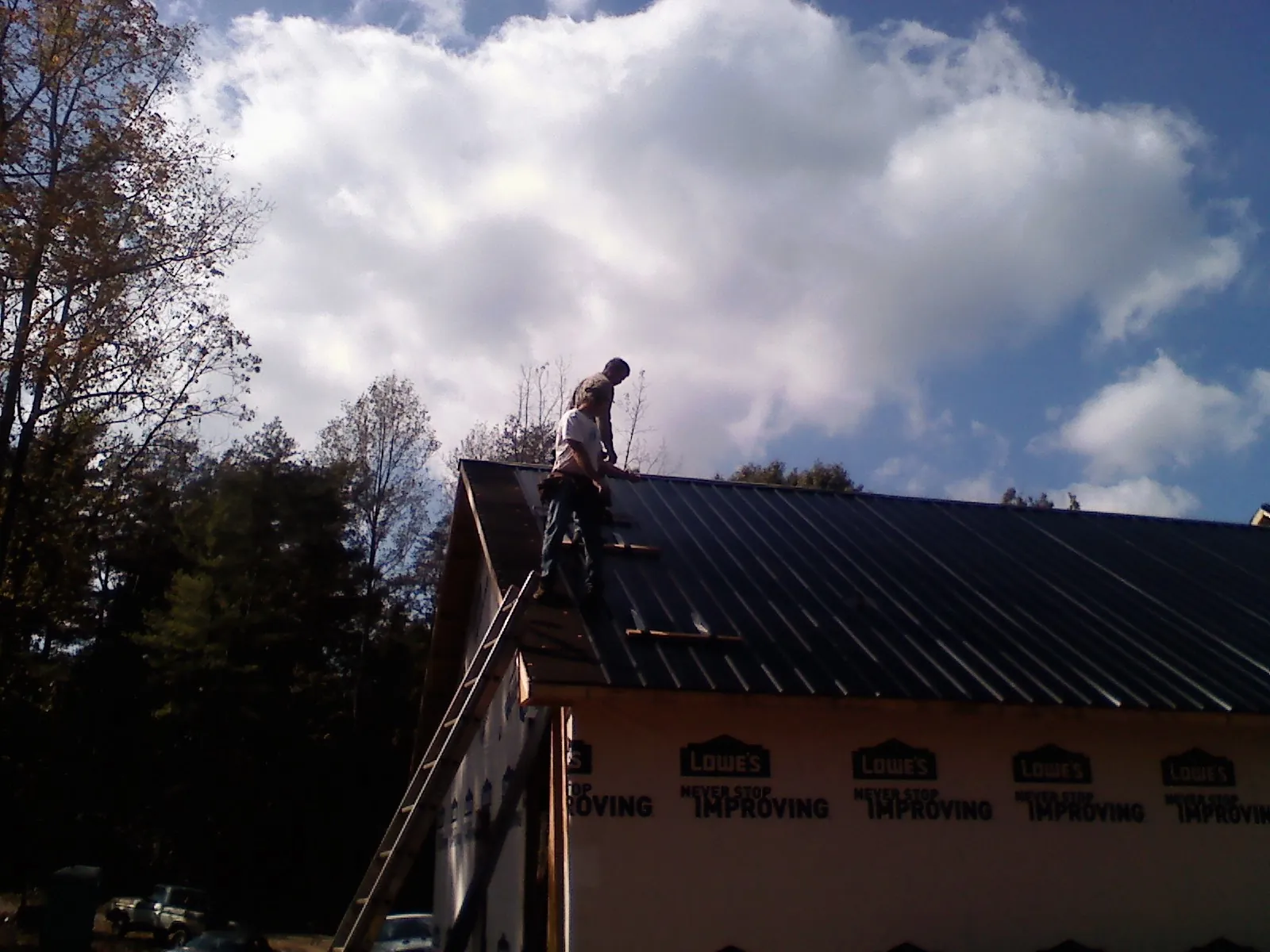 Roofer fastening dark metal panels high against a cloudy sky, from a Roof Inspection job in Iota
