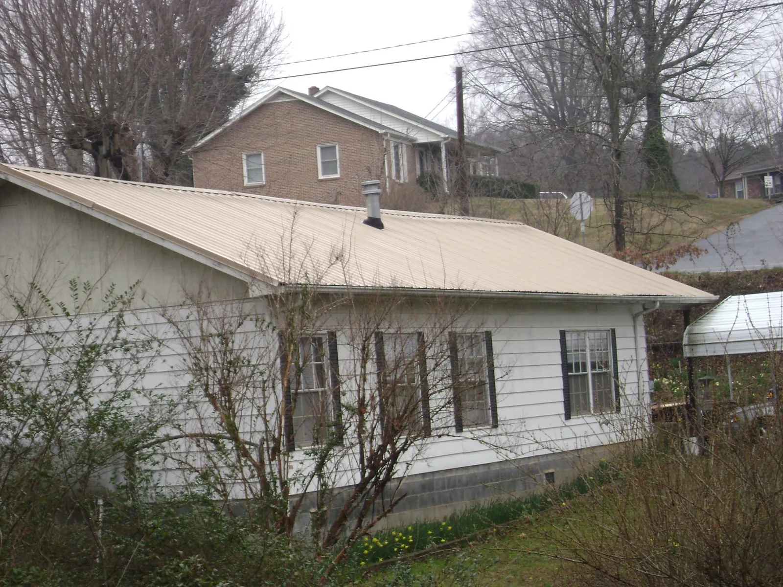 Tan metal roof on a white sided house set into a hillside — Commercial Roofing by Roofing Brothers in Iota