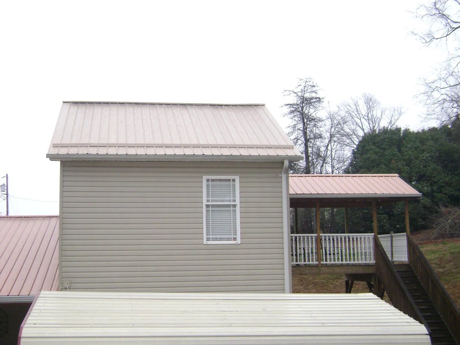 Tan metal roofs on a two story addition and attached porch, from a Roof Replacement job in Iota